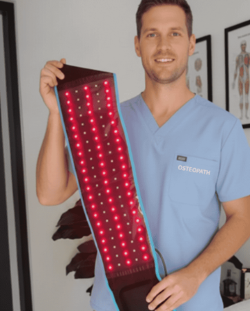 Person in blue scrubs holding a red light therapy device